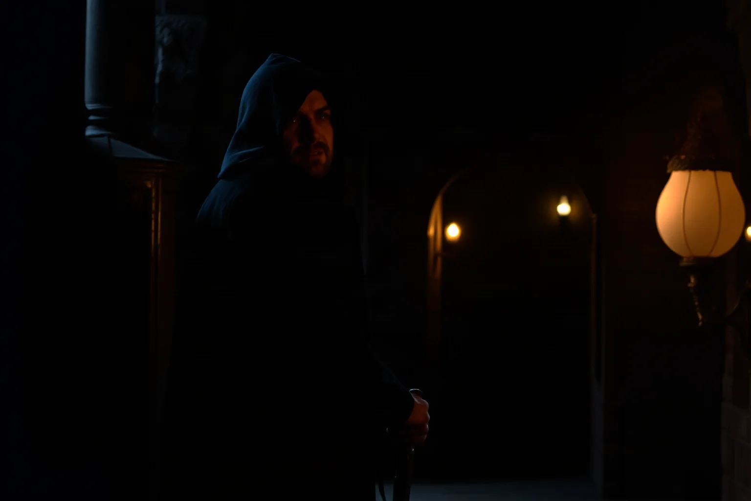 A shadowy hooded figure sneaking through a torch-lit castle corridor, representing the insult 'Knave'