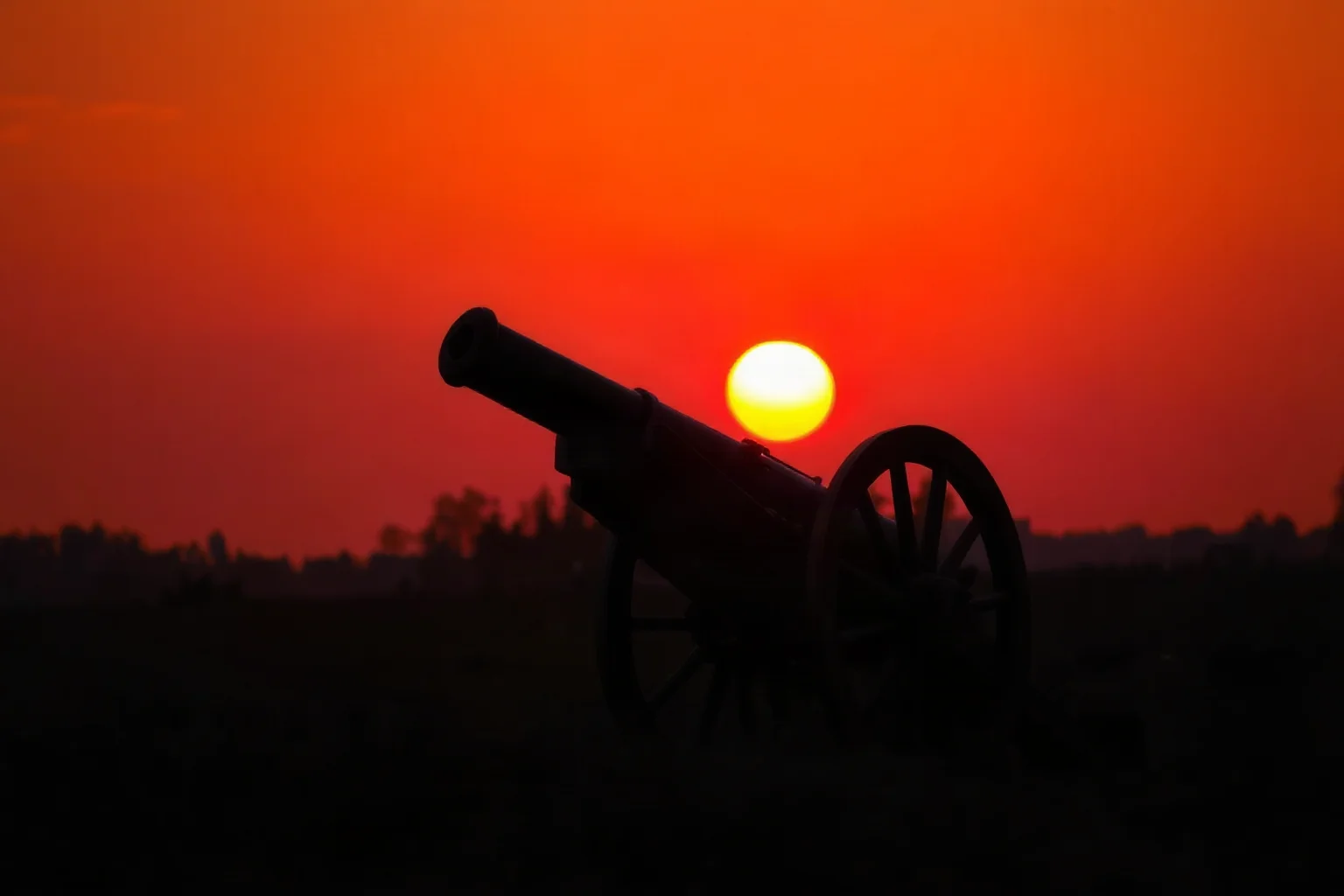 A silhouette of a Civil War-era cannon against a smoky orange battlefield sunset