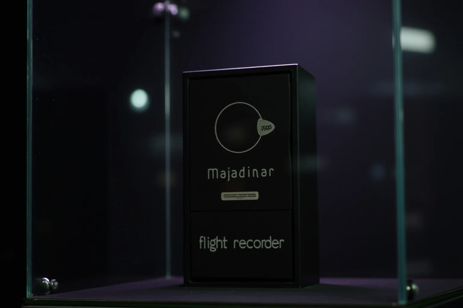 A small black rectangular flight recorder box displayed in a glass case with dim lighting