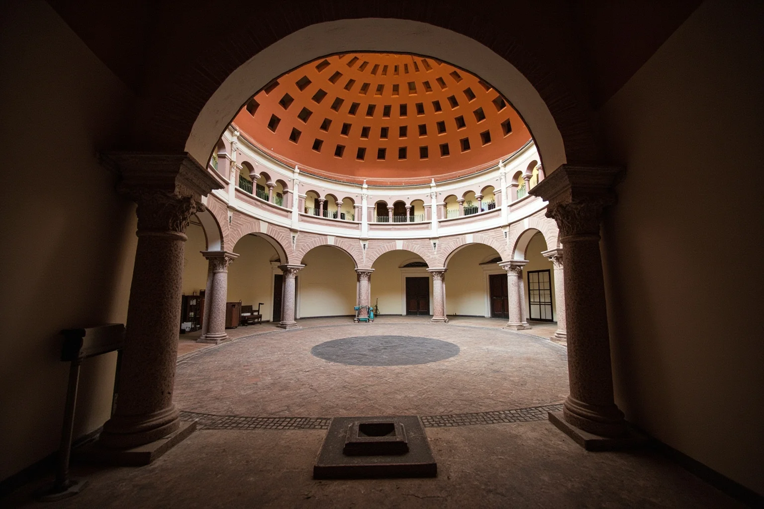 A small domed chapel courtyard with terracotta roundels and a coffered dome ceiling, early morning light