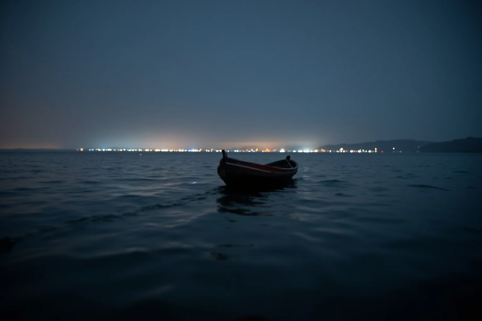 The Most Daring Prison Escapes in History 18 A small wooden rowboat crossing dark open water toward distant coastal lights