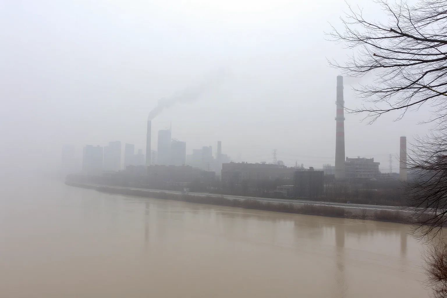 A smoke-filled industrial skyline with polluted river water nearby