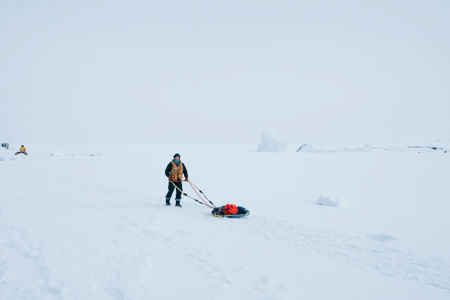 A solitary explorer trekking across a vast icy Antarctic plateau pulling a sled