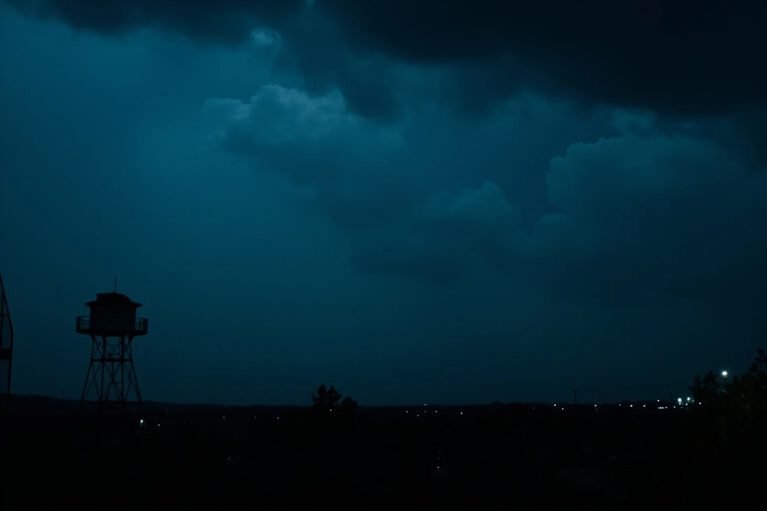 25 Disturbing Last Words By Notorious Criminals 9 A stormy night sky over a prison silhouette, dramatic clouds suggesting chaos and unrest, distant watchtower lights