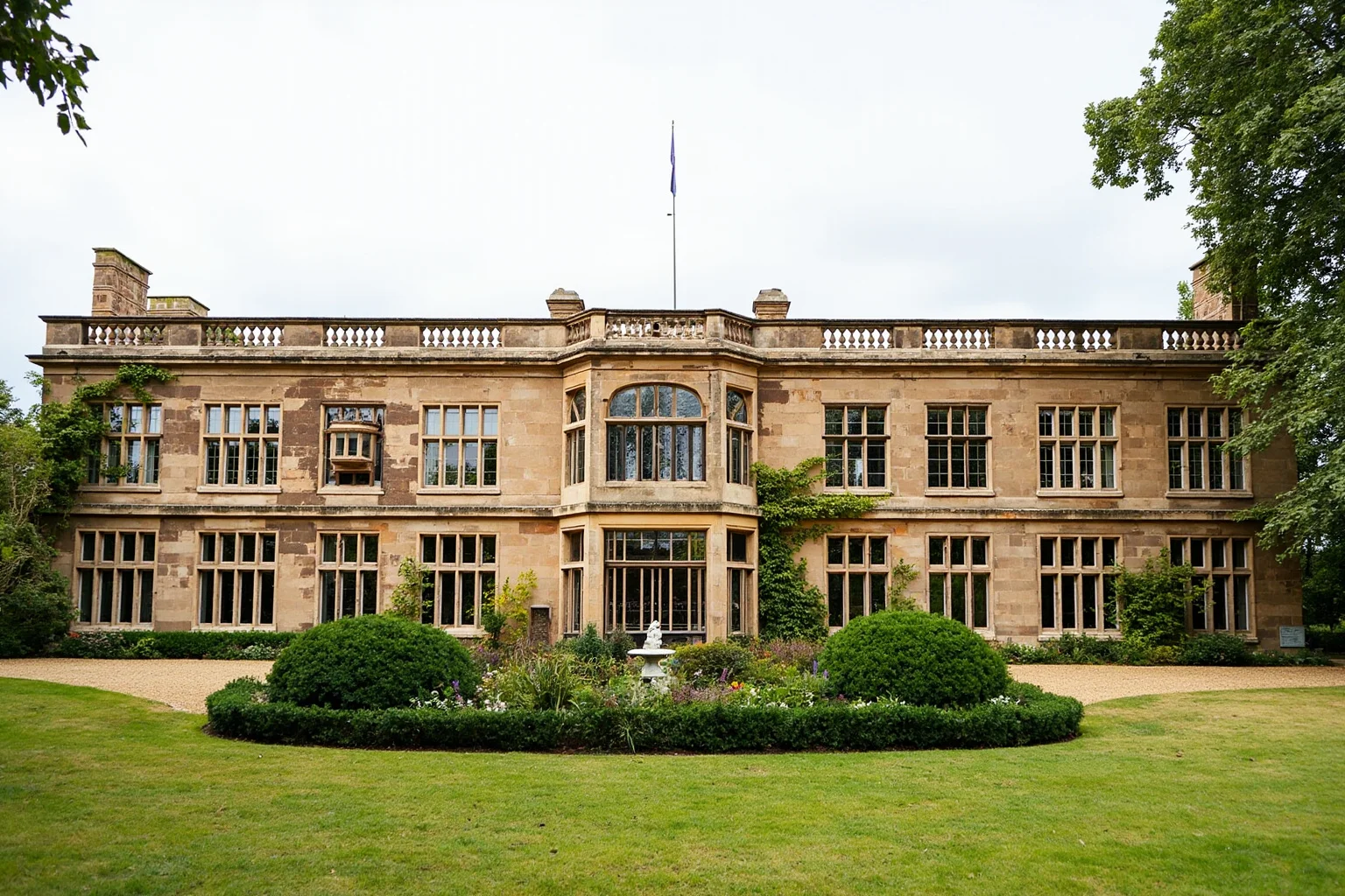 A symmetrical English Renaissance country house with large mullioned windows and manicured gardens