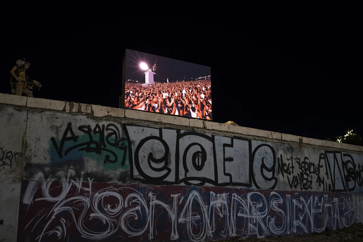 Most Important Historical Events Televised Live 14 A television screen showing jubilant crowds atop a large graffiti-covered concrete wall at night, chipping away pieces