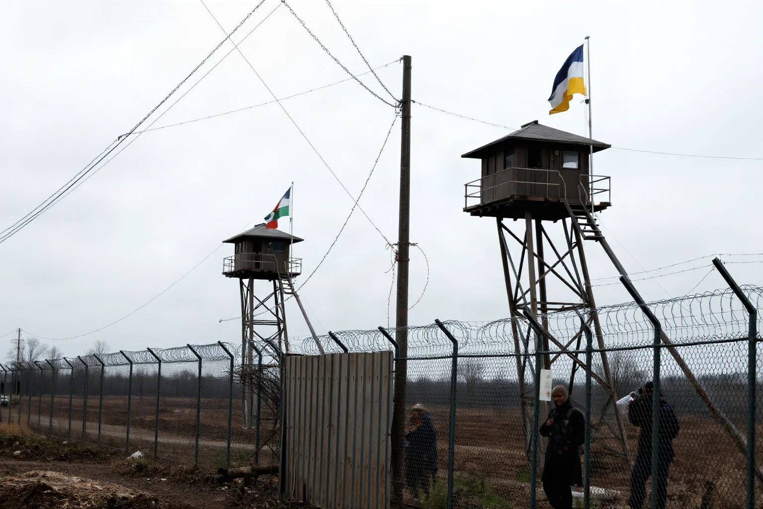 A tense demilitarized border checkpoint with barbed wire and watchtowers under overcast skies