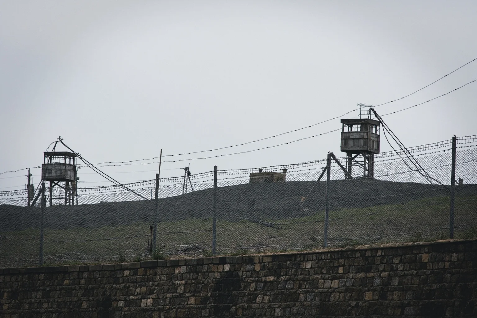 Wars That Lasted A Lot Longer Than You Thought 22 A tense fortified border with barbed wire and watchtowers under a gray sky, symbolizing an unresolved armistice