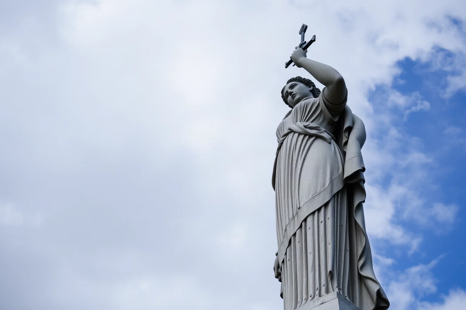 A towering concrete statue of a woman striding forward holding a raised sword, dramatic sky background