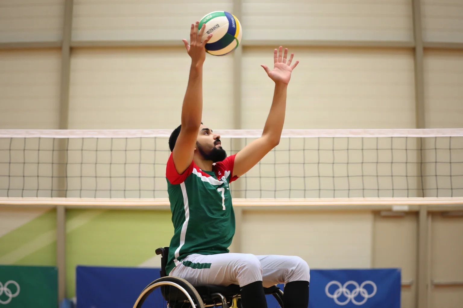 A very tall Iranian Paralympic athlete in sitting volleyball uniform demonstrating reach advantage