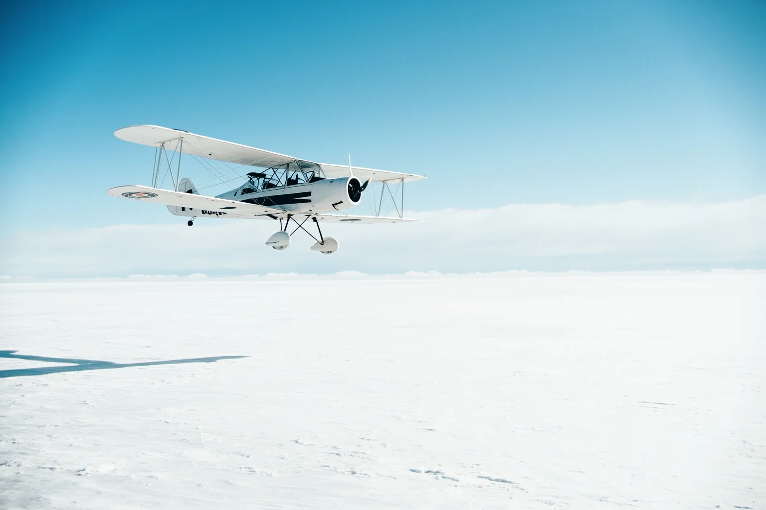 A vintage biplane flying low over a vast white polar ice cap under a bright sky