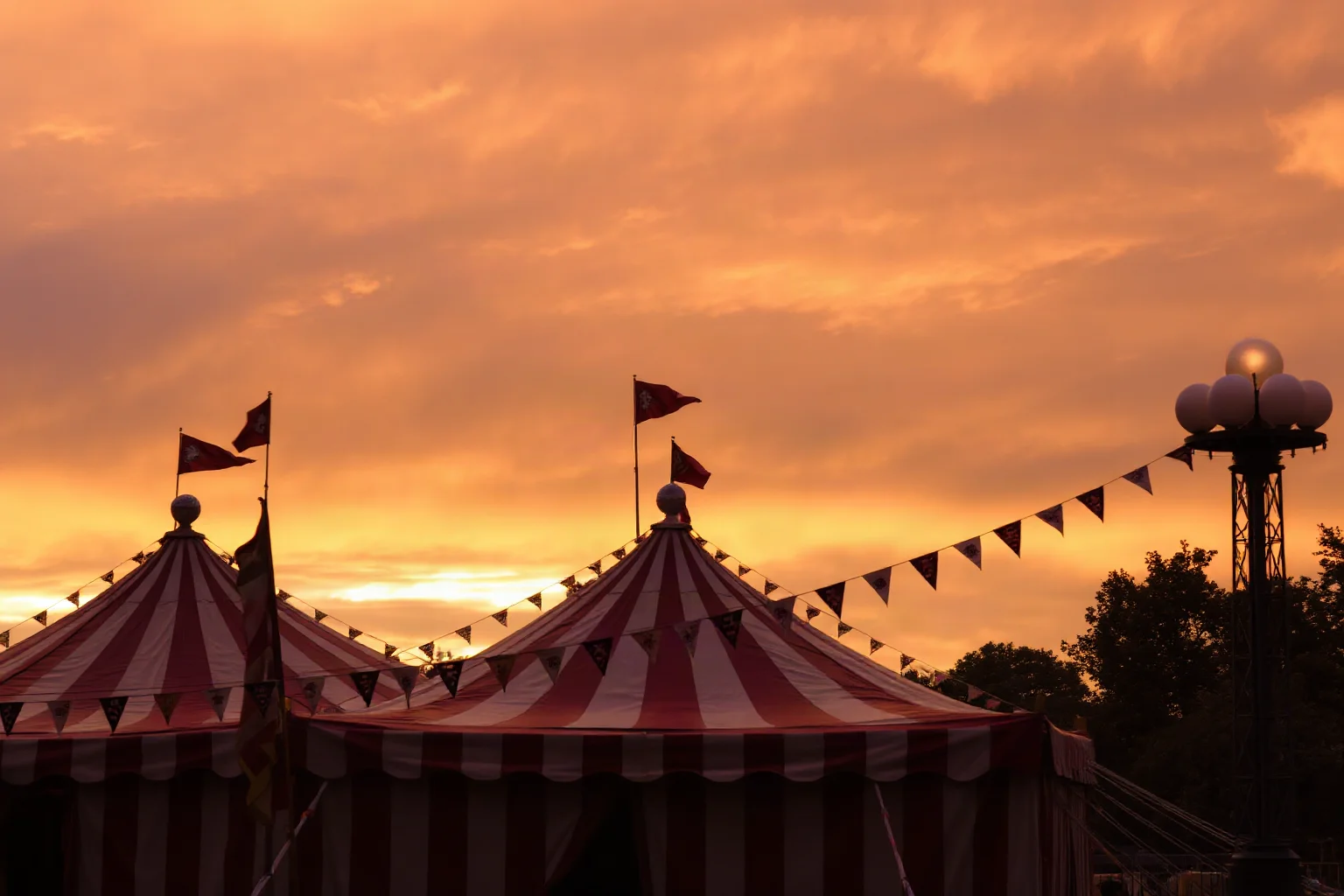 A vintage carnival tent and sideshow banners under a dusky orange sky