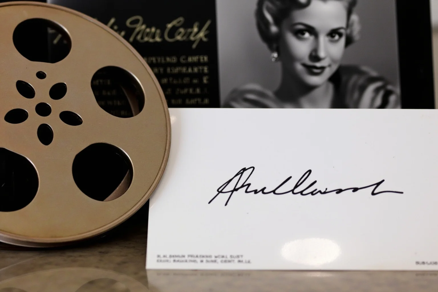 A vintage Hollywood film reel and glamorous black-and-white photograph displayed with an autograph card
