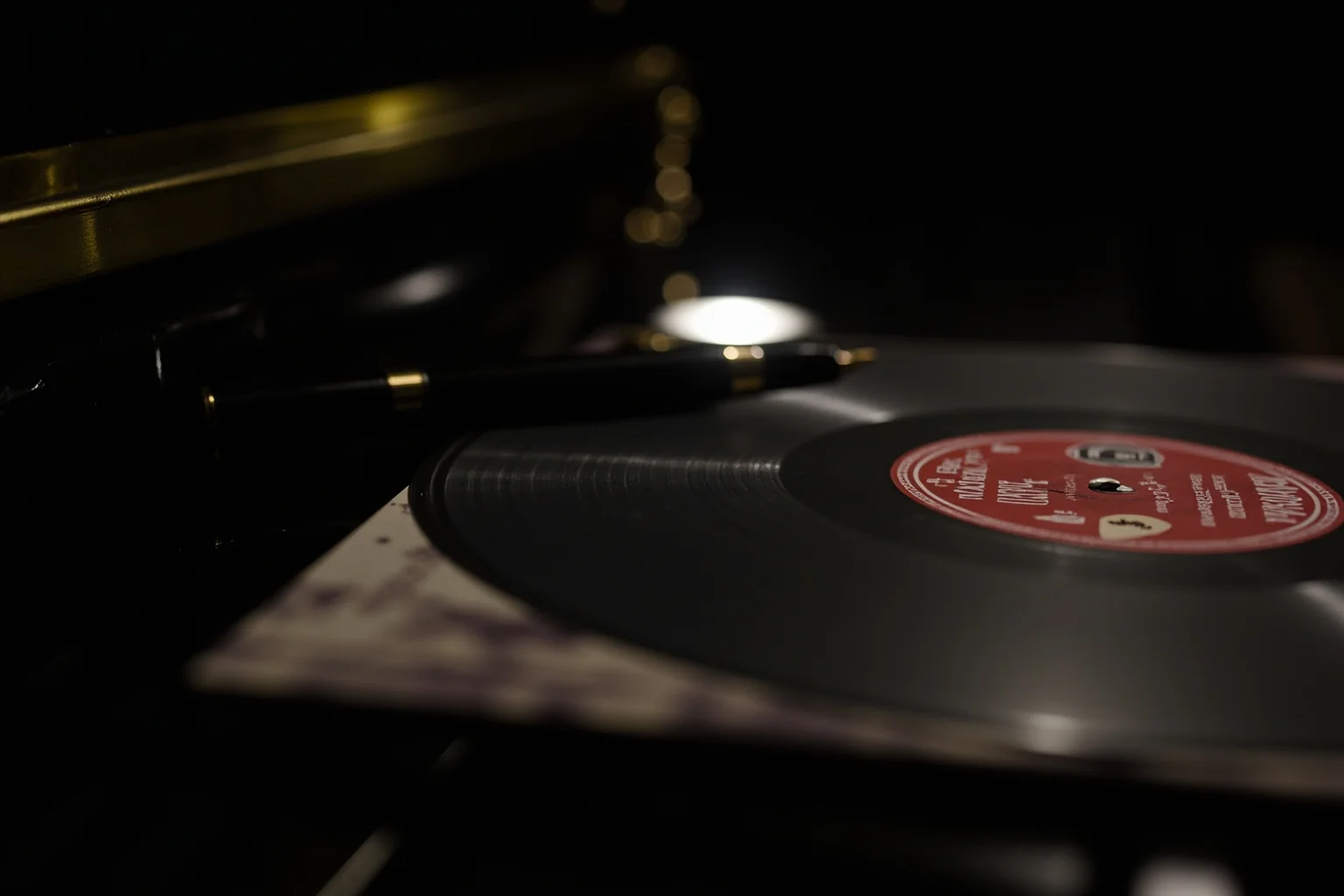 A vinyl record album cover resting on a piano beside a fountain pen and a dimly lit spotlight