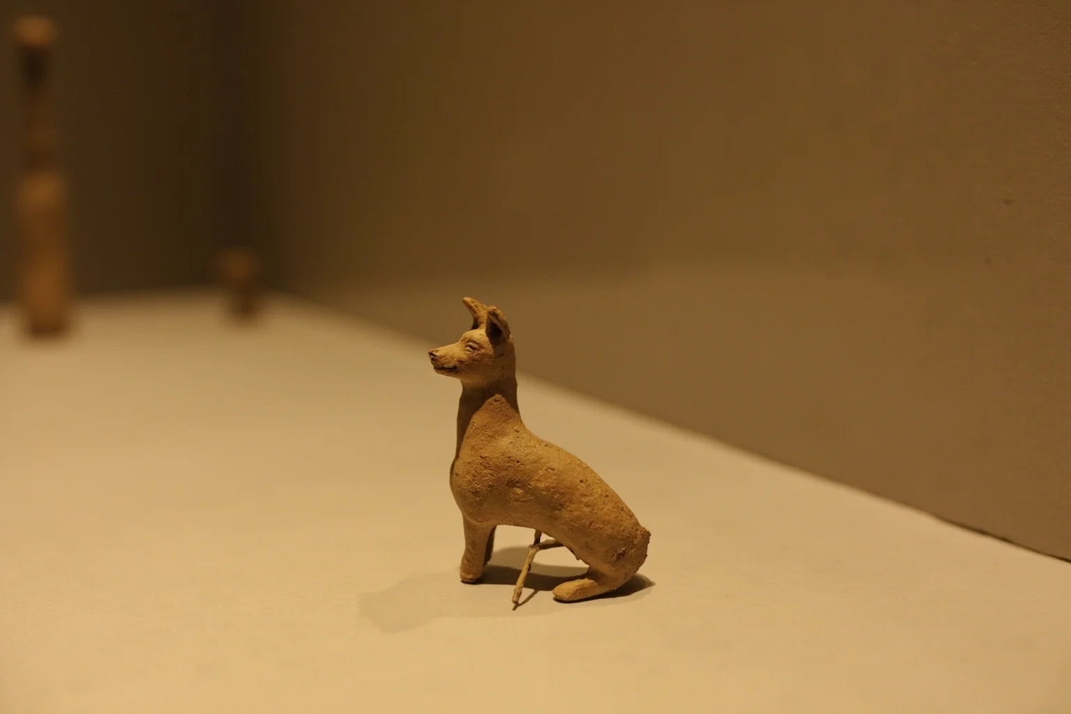 Pooches of the Past: 23 Extinct Dog Breeds and Their Stories 6 A weathered ancient clay figurine of a small dog, displayed as an archaeological artifact on a museum shelf