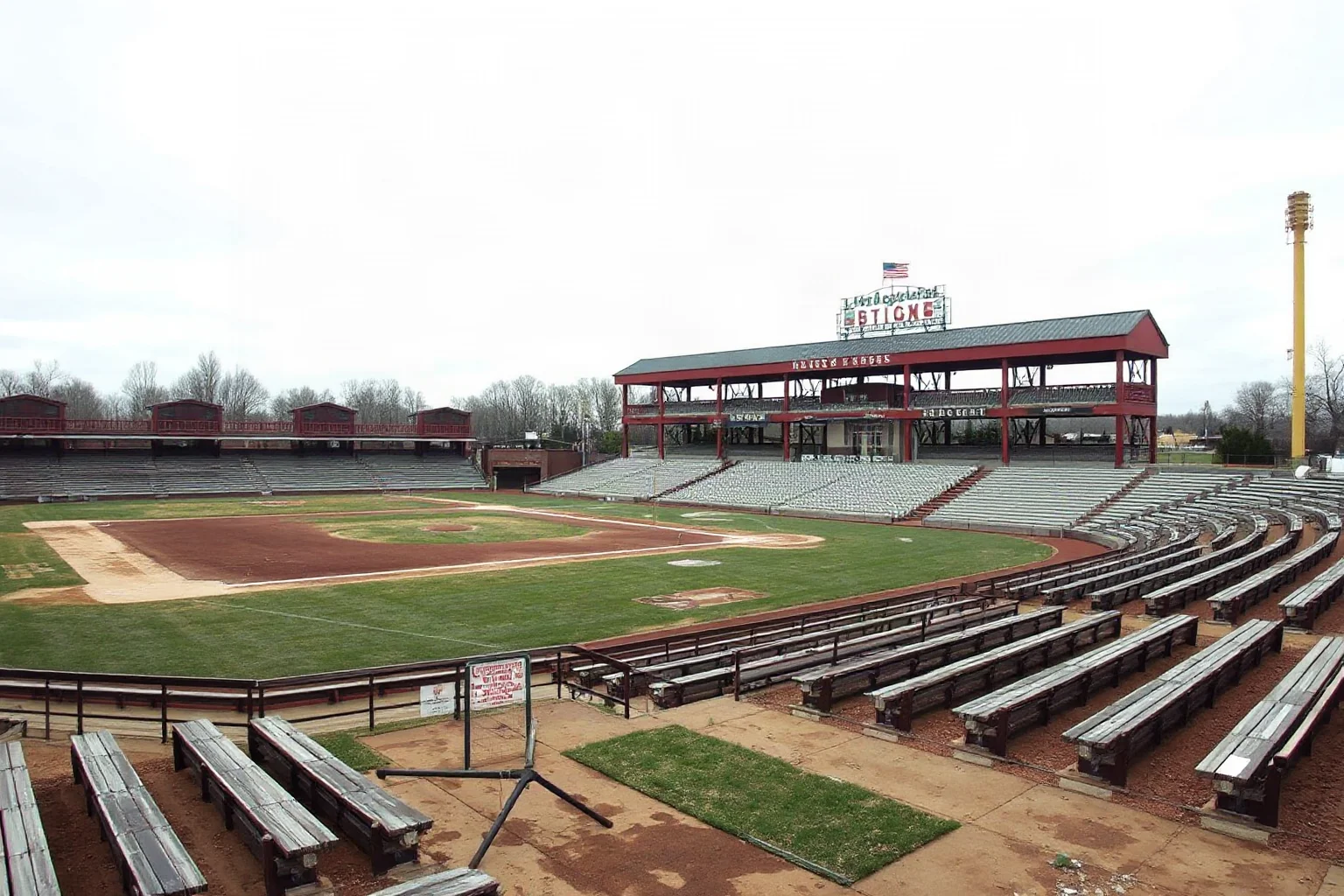 A weathered minor league baseball park from the early 1900s with wooden bleachers and a small traveling team