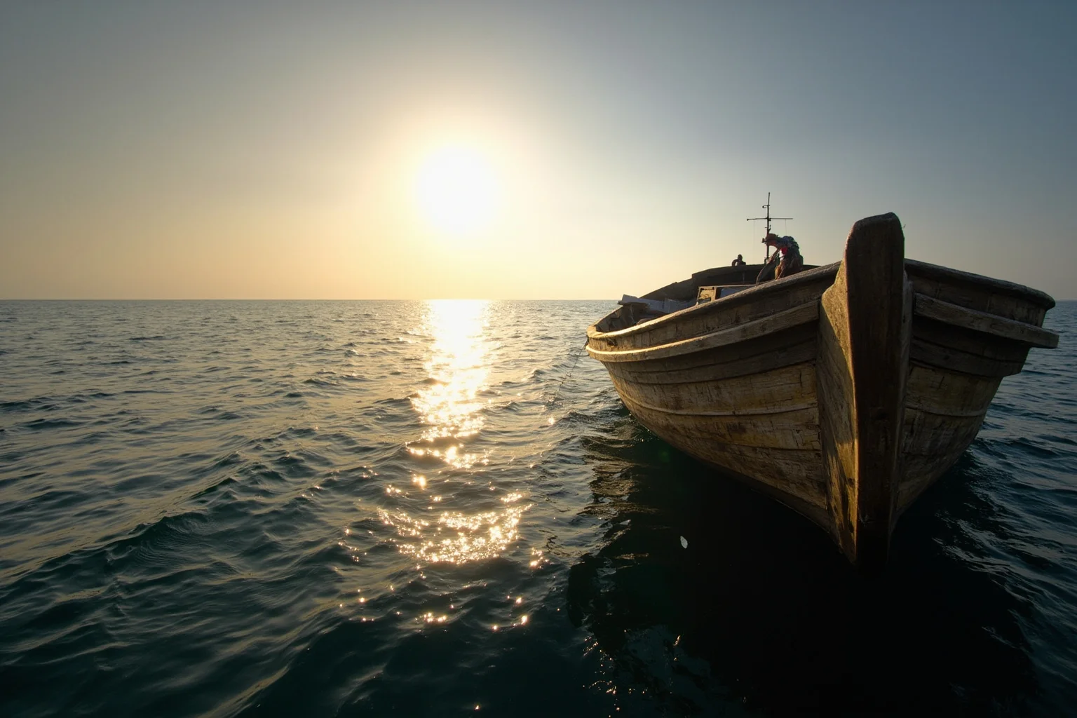 A weathered wooden fishing boat adrift on open ocean under a blazing sun