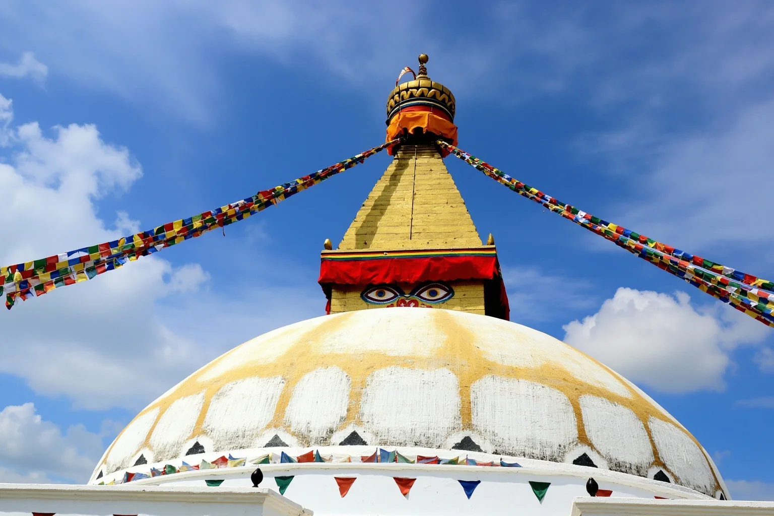 A whitewashed dome-shaped stupa decorated with painted eyes and prayer flags
