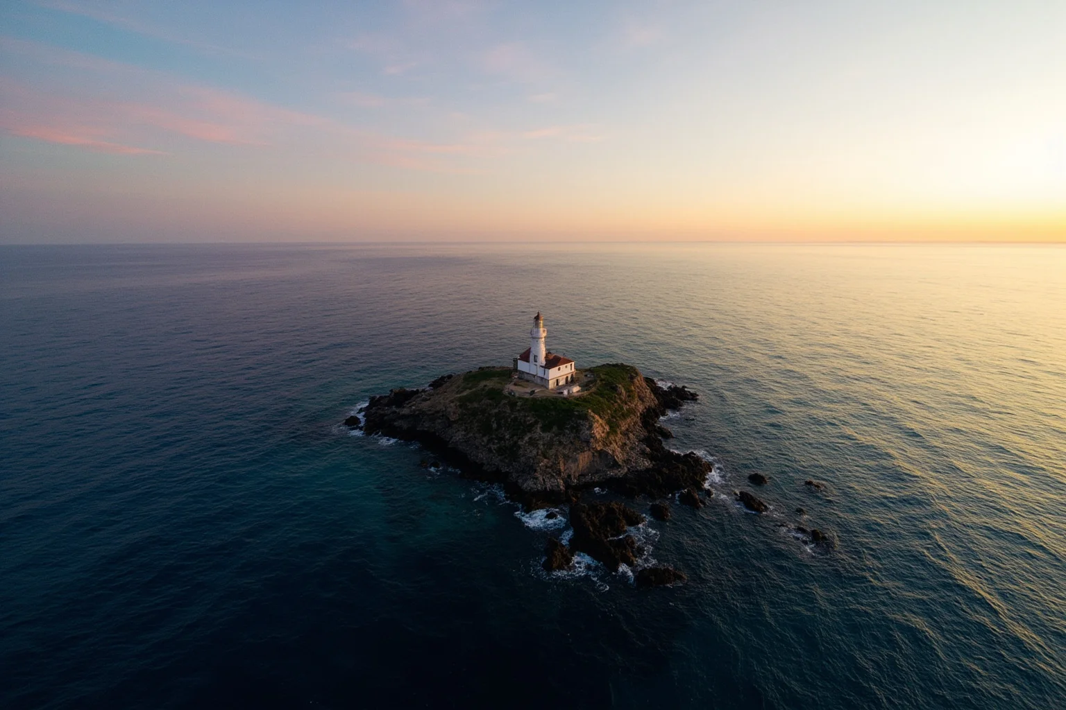 A wide aerial view of a small isolated lighthouse island surrounded by open ocean at sunset
