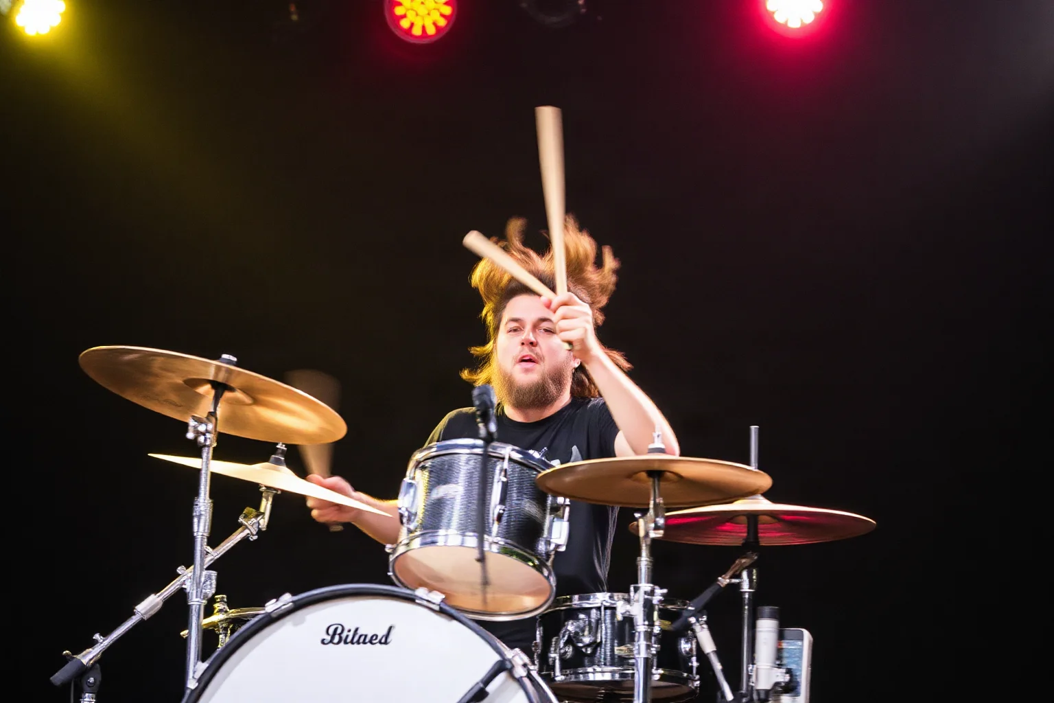 A wild, energetic drummer captured mid-motion with drumsticks flying, chaotic stage backdrop