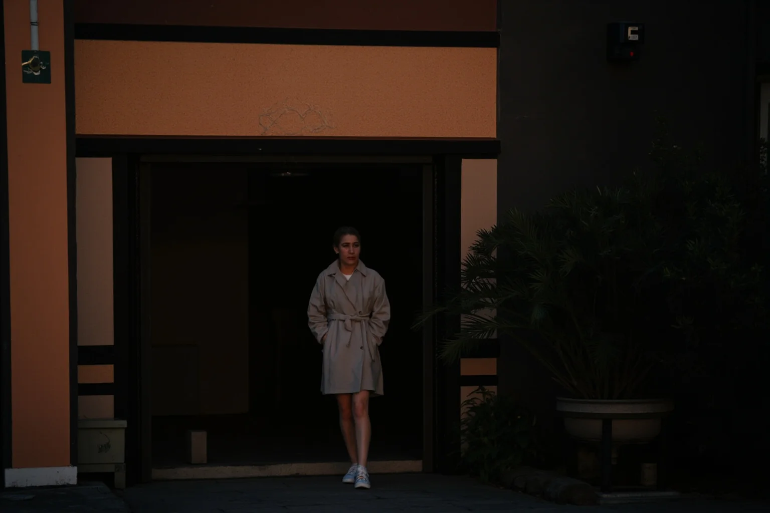 A woman in plain coat quietly entering a hospice at dusk, unaccompanied by press or cameras