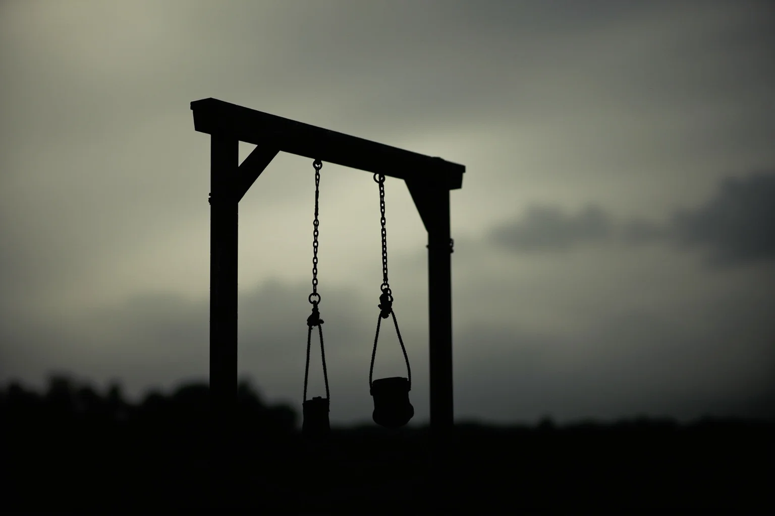25 Disturbing Last Words By Notorious Criminals 3 A worn 1930s prison gallows silhouette against a gray dawn sky, stark and atmospheric, no identifiable figures