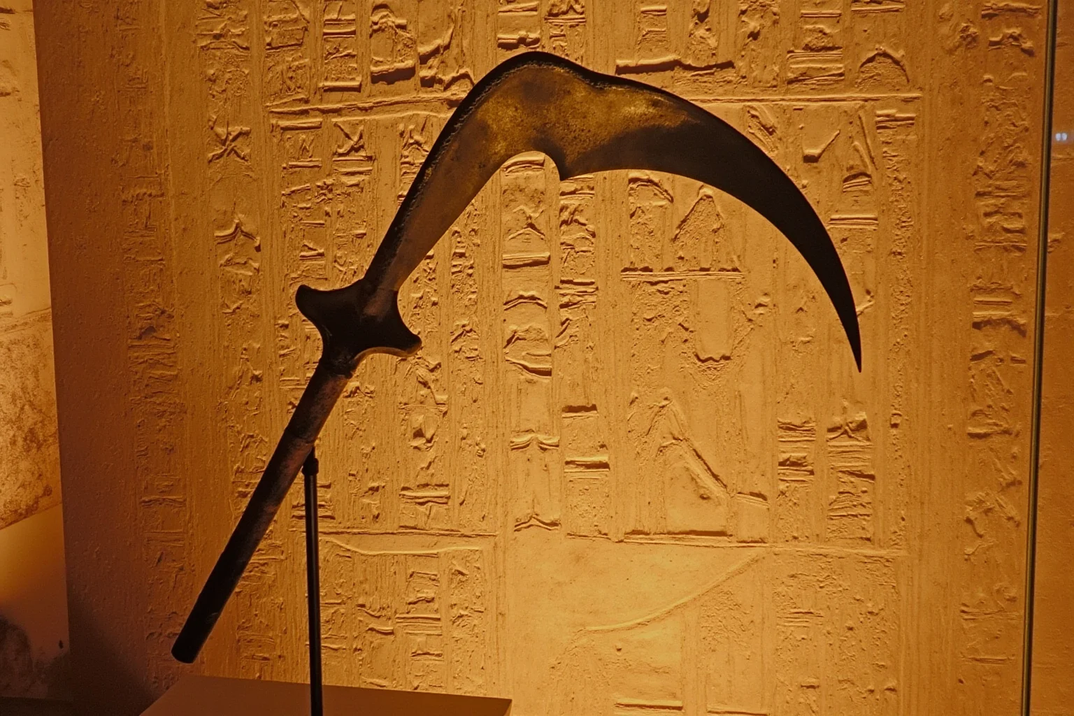 An ancient Egyptian curved sickle-sword displayed near hieroglyphic tomb wall carvings