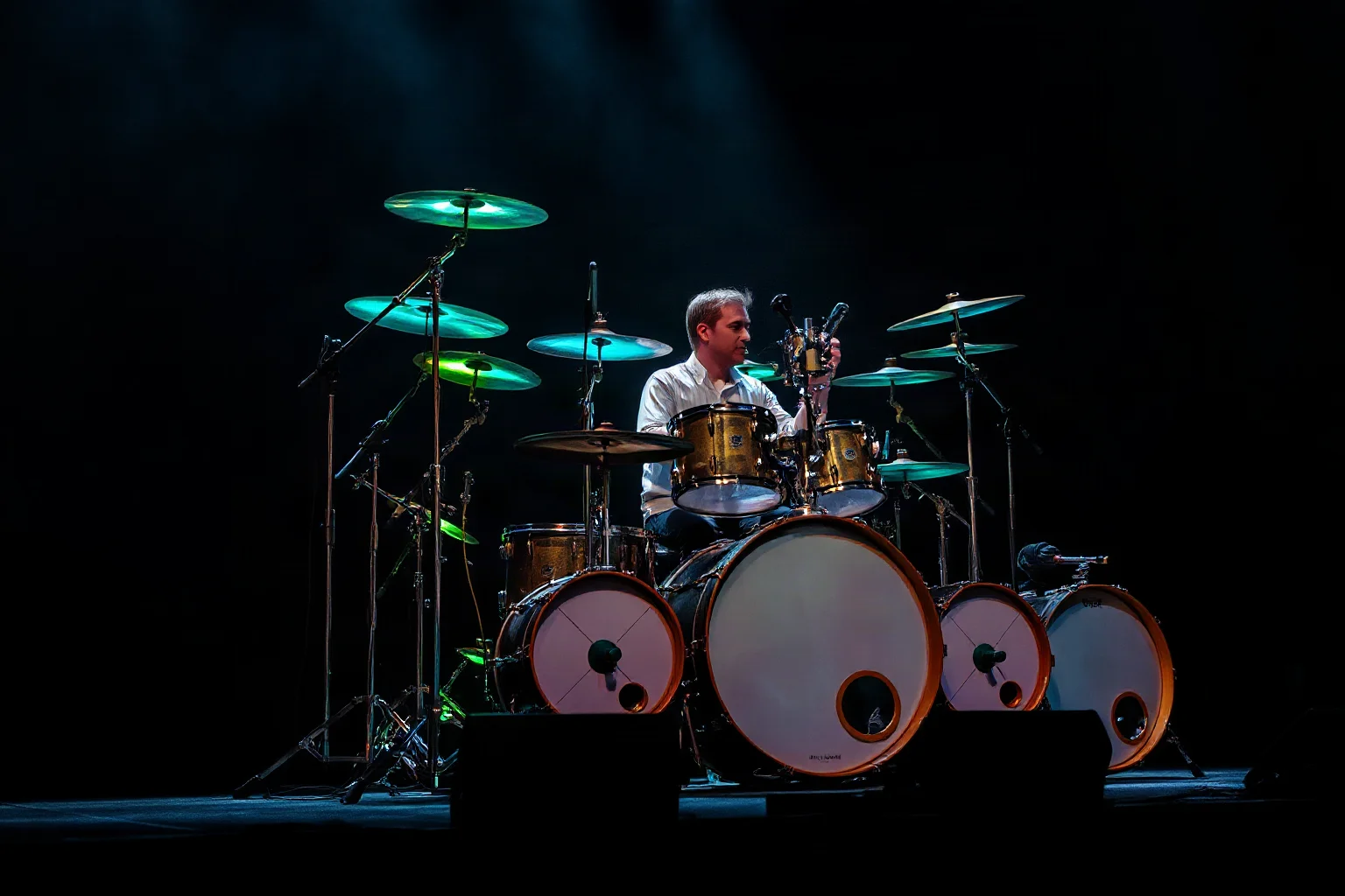 An avant-garde drummer with an enormous custom multi-tiered drum and percussion setup on a dark stage
