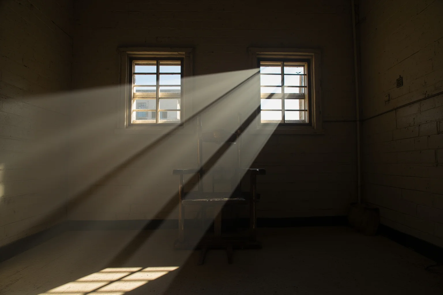 25 Disturbing Last Words By Notorious Criminals 4 An empty electric chair room in an old prison, dust in the air, dramatic side lighting, vintage 1980s institutional decor