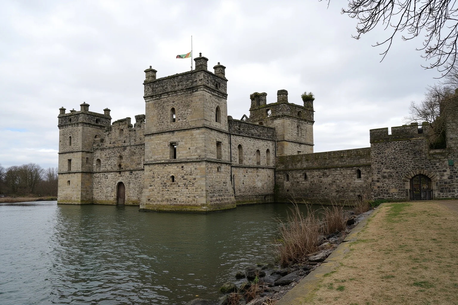 An imposing medieval stone tower fortress beside a river, with battlements and a moat