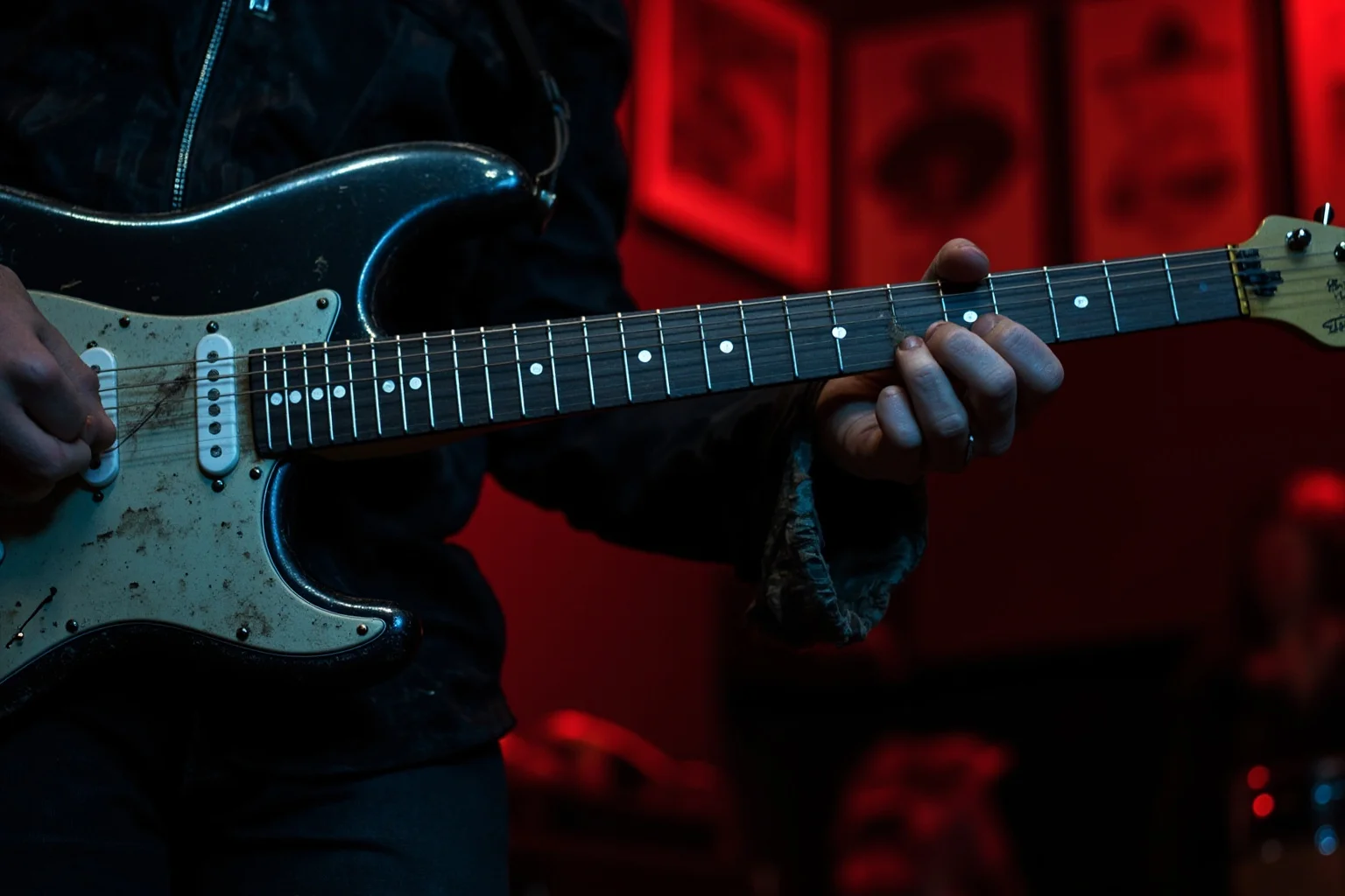 An Irish blues-rock guitarist playing a worn, road-tested Stratocaster-style guitar on a small pub stage, raw energetic performance
