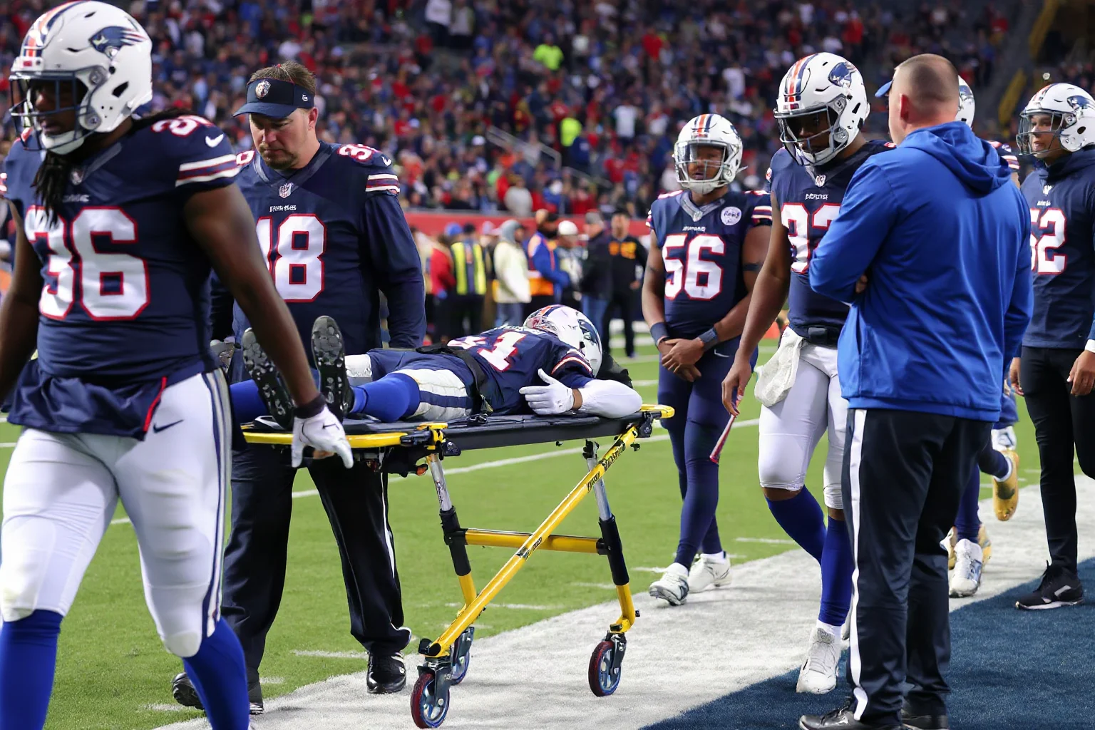 An NFL player on a stretcher being carefully carried off the field by medical staff, teammates lined up respectfully