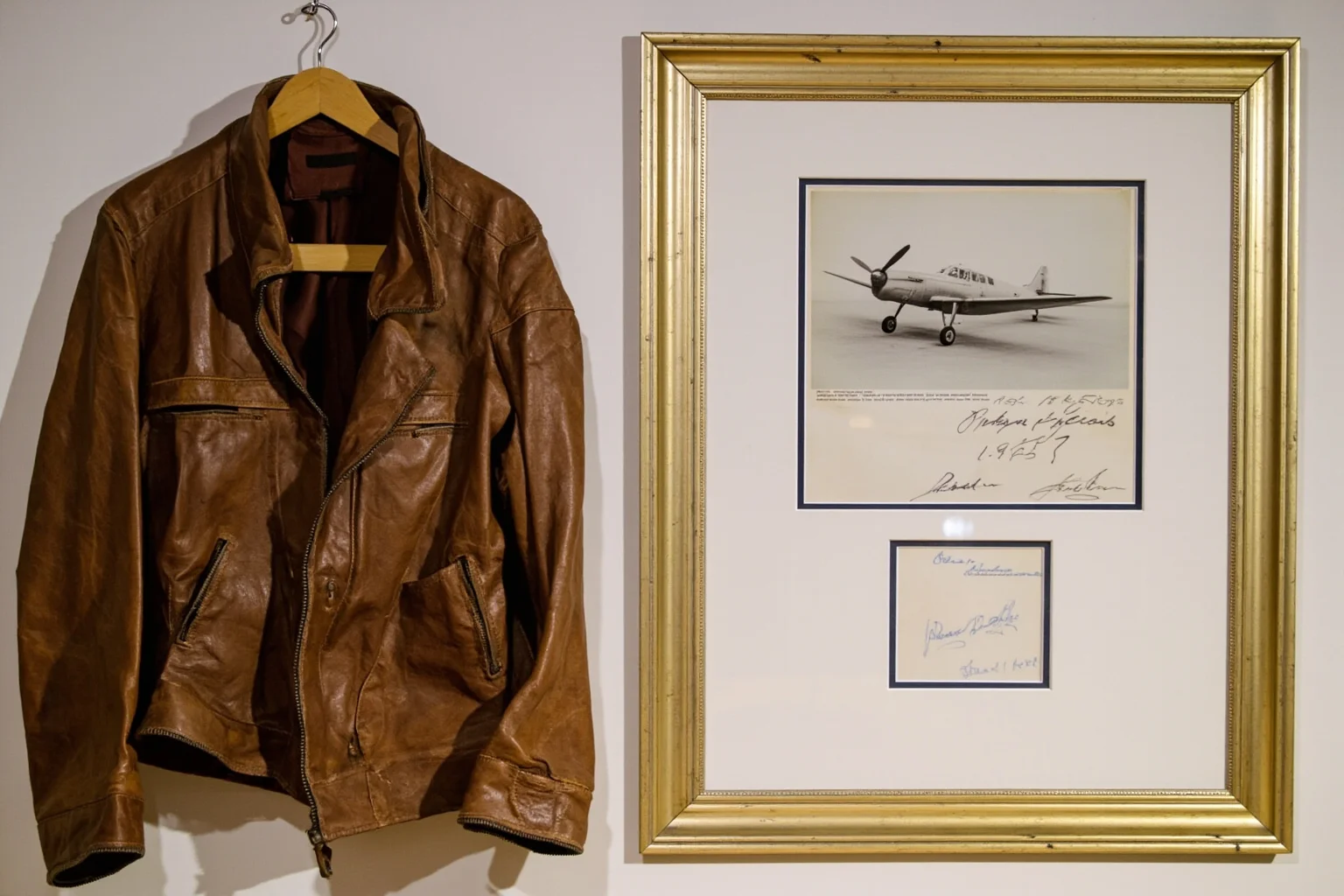 An old aviation leather jacket and vintage propeller plane photograph displayed with a framed signed document