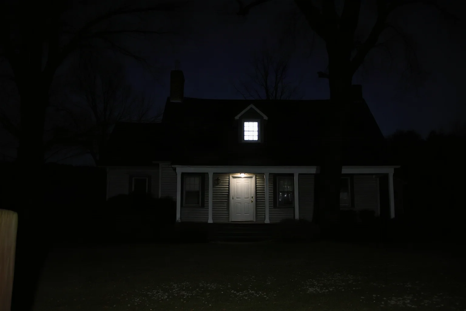 An old New England farmhouse at night with a single lit upstairs window