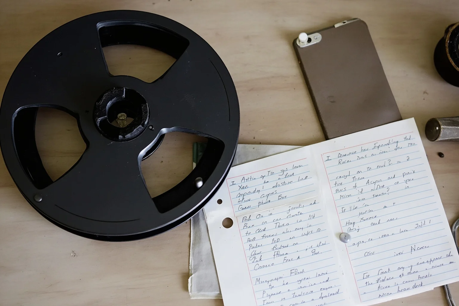 An old reel-to-reel tape recorder next to handwritten notes, representing archival audio recordings later reviewed by researchers
