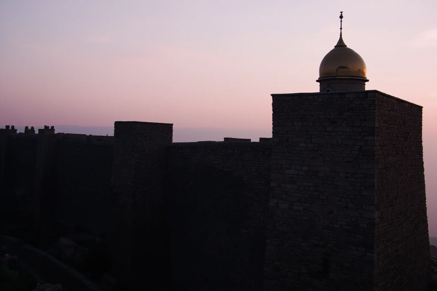 An old stone city wall with a golden dome visible at dusk