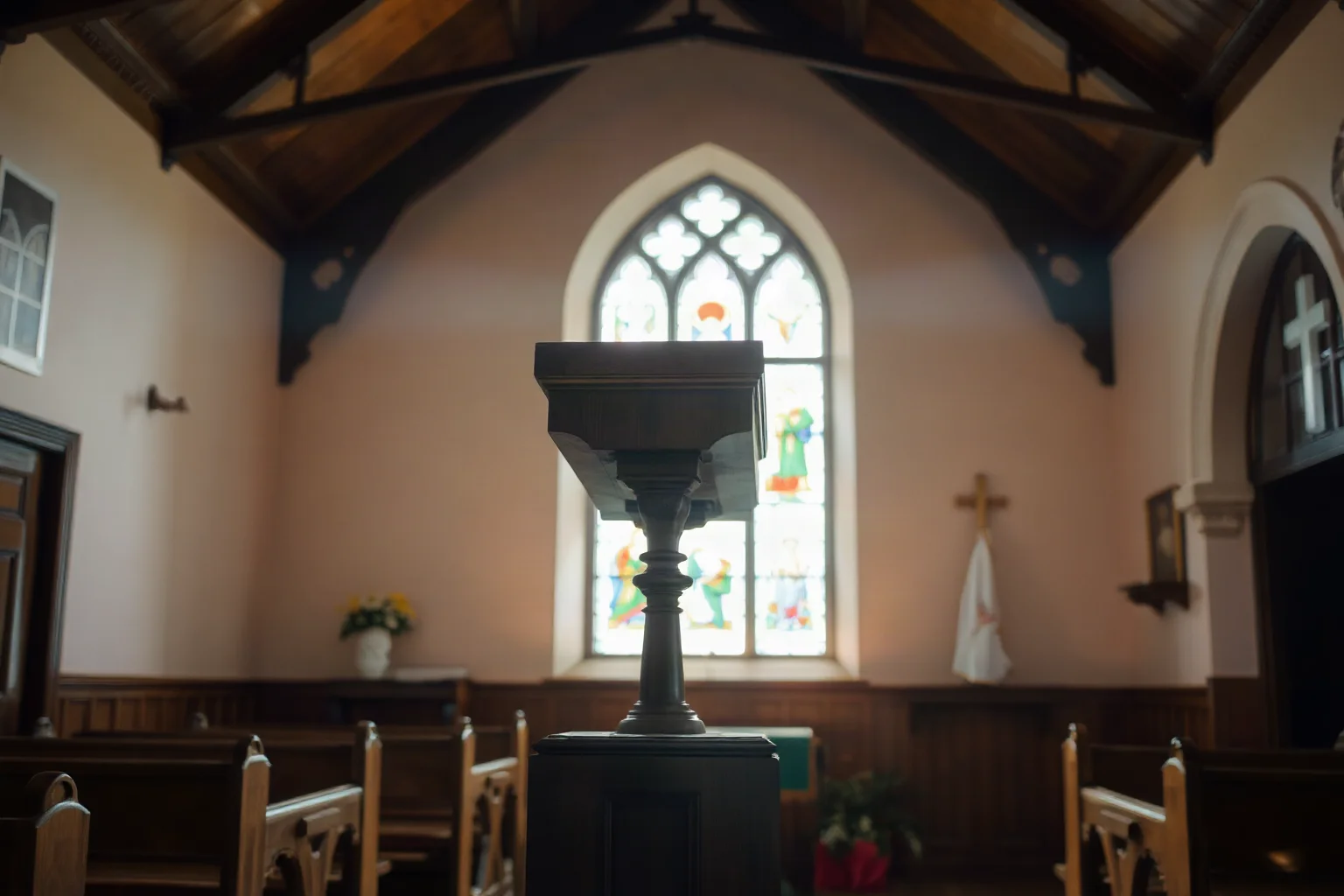 An old wooden pulpit inside a chapel with soft light streaming through a stained glass window