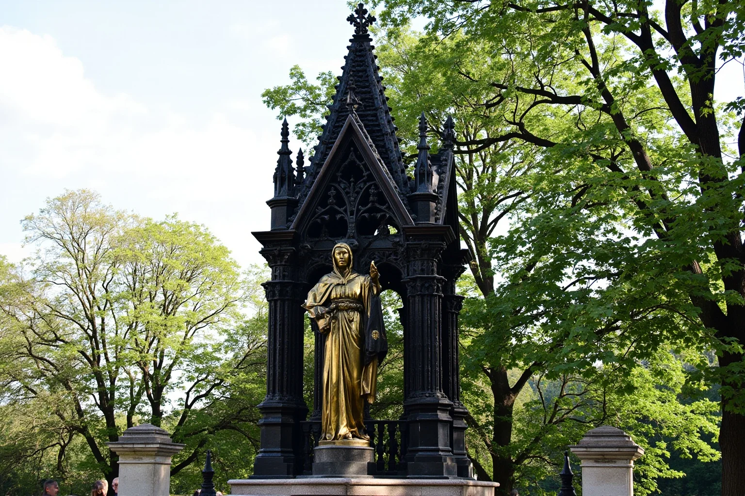 An ornate gothic memorial monument with gilded statue in a London park setting