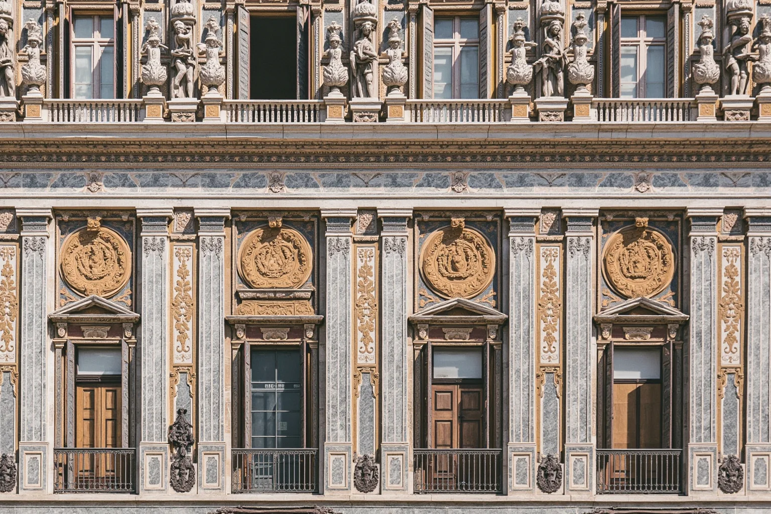 An ornate marble monastery facade densely covered in classical sculpture and inlaid stonework