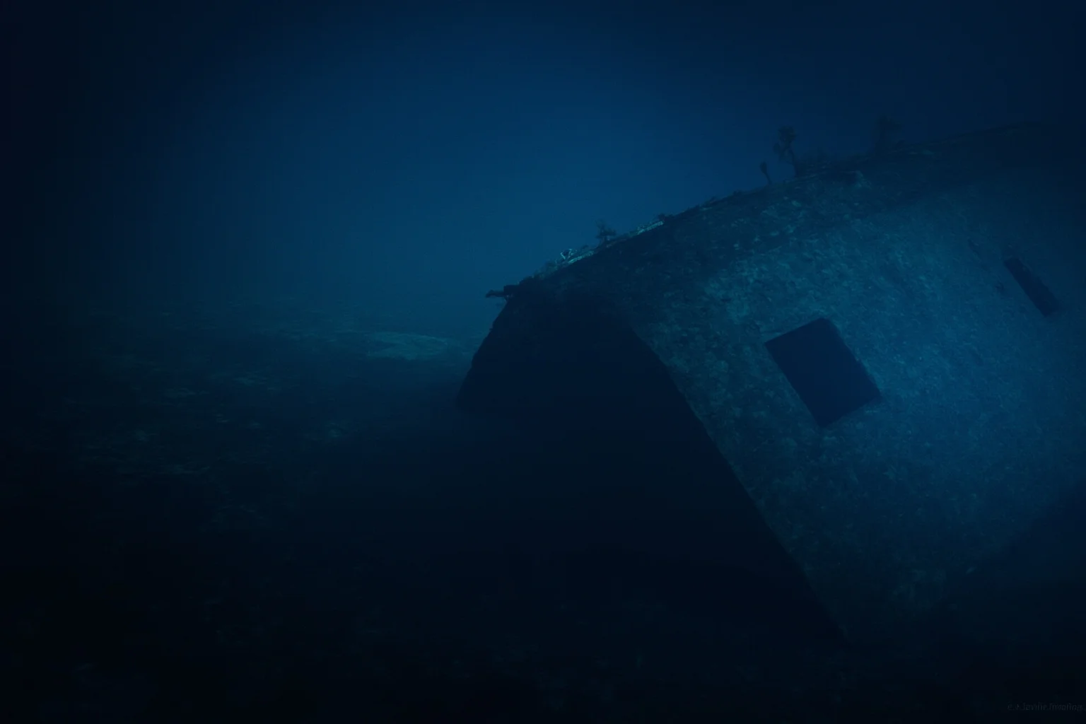An underwater shipwreck scene with a sunken vessel resting on the seabed, dim blue light
