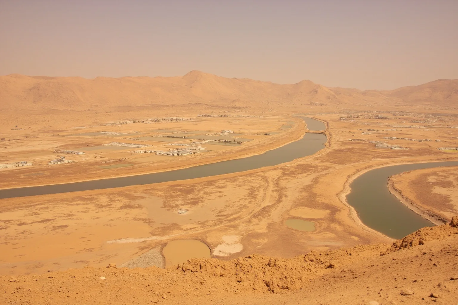 Ancient desert oasis settlement with irrigation channels fading into windblown sand