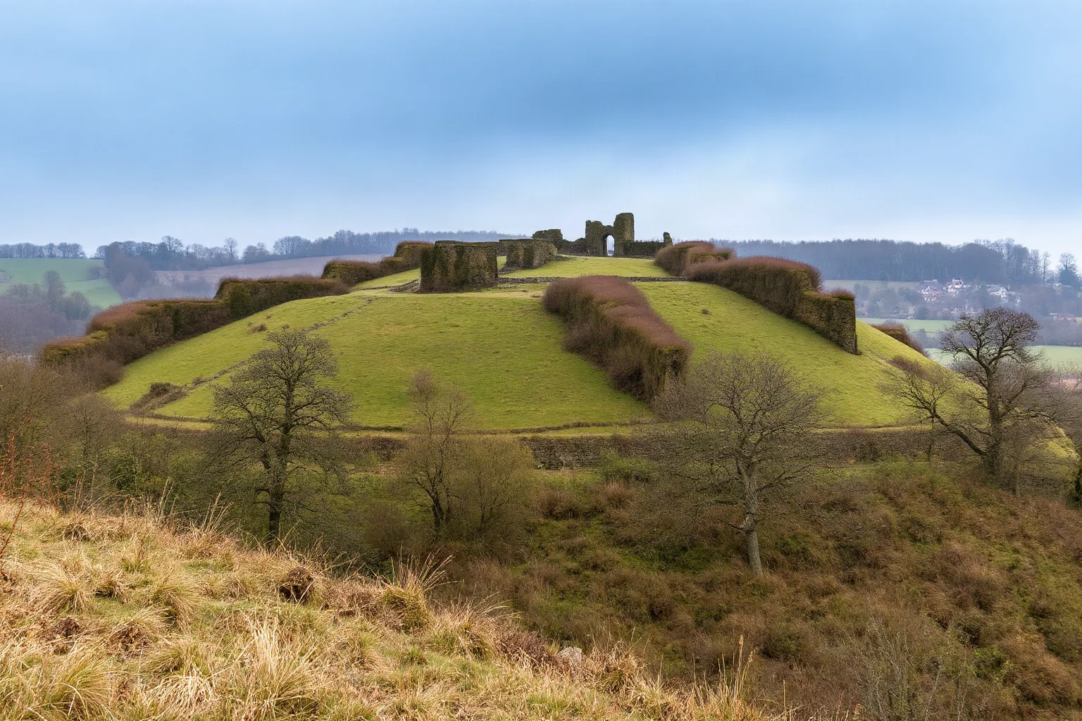 Atmospheric hillside mound ruins of Old Sarum with ancient earthwork fortifications and overgrown vegetation in English countryside