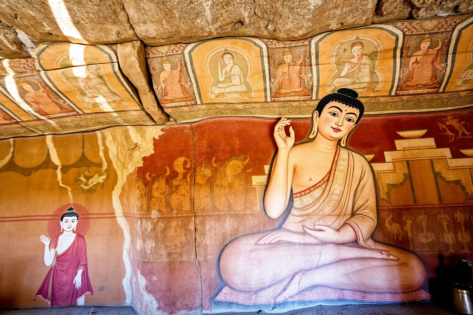Buddhist cave wall murals with intricate painted figures and patterns in earthy tones, showing ancient oil-based pigment technique