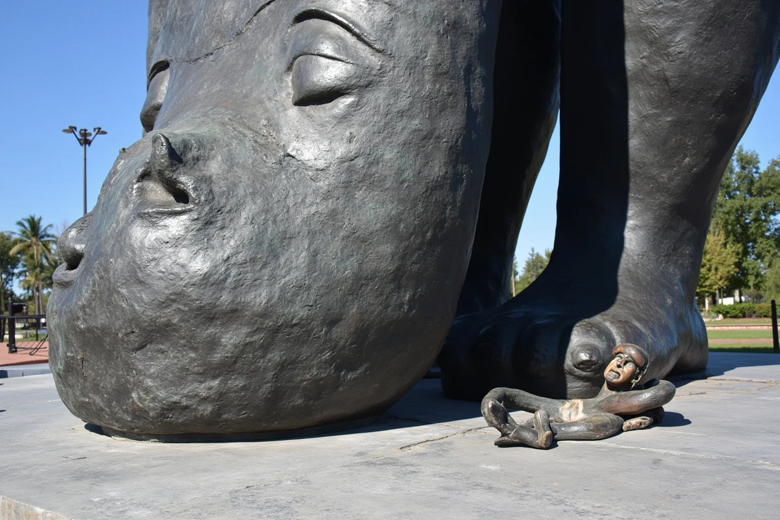 Close-up of a monumental bronze relief sculpture showing its massive scale compared to small human figures nearby