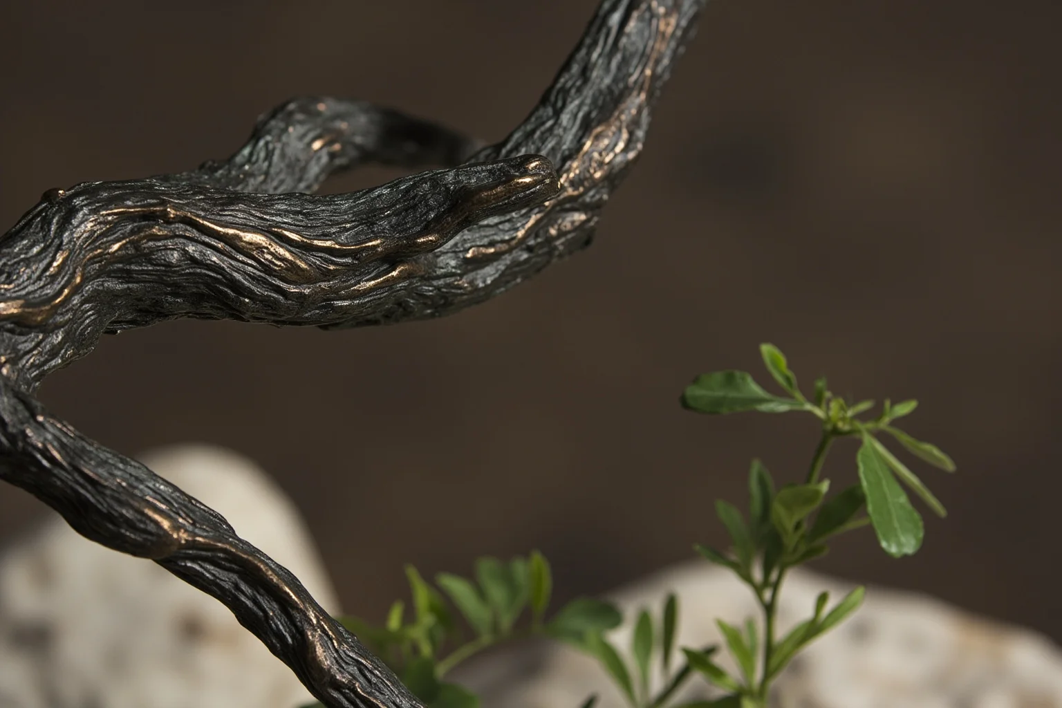 Close-up of a sculpted dead tree branch beside a small sprouting green branch in bronze and stone
