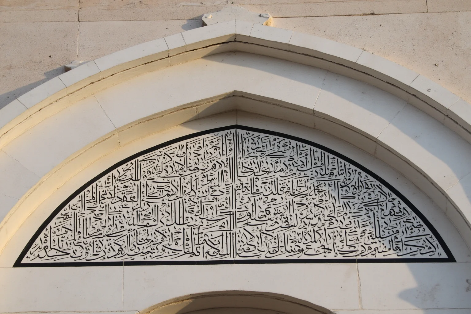 Close-up of elegant black calligraphy inlaid into a white marble archway, historical Islamic art style