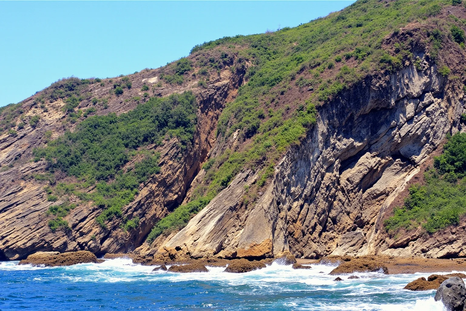 Coastal cliffs on a small island crumbling into the sea with fossil-bearing rock layers visible