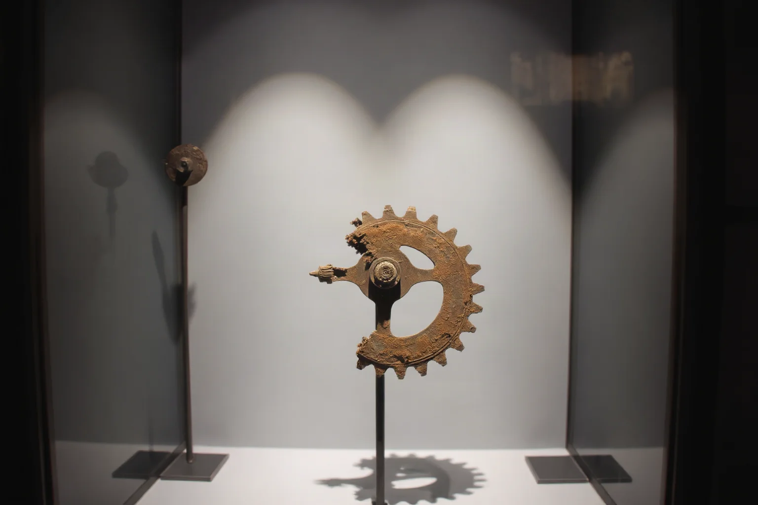 Corroded bronze geared mechanism fragment displayed under museum glass