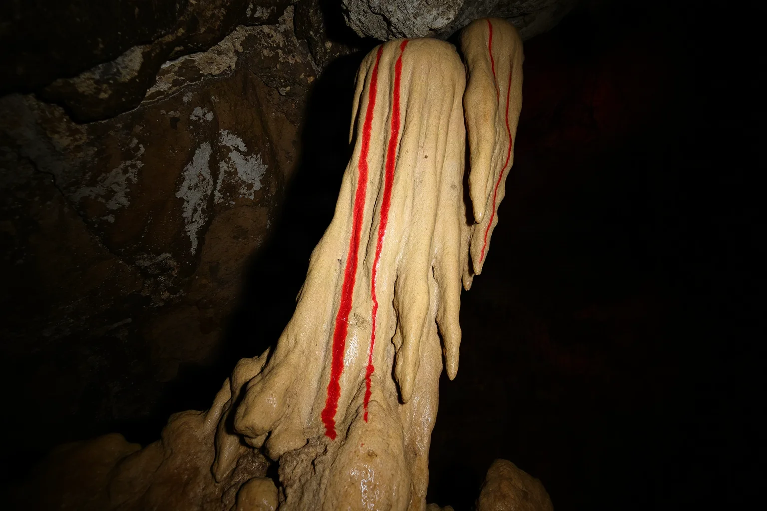 Deep cave interior with red ochre pigment marks on a stalagmite formation, cave wall texture and mineral deposits visible