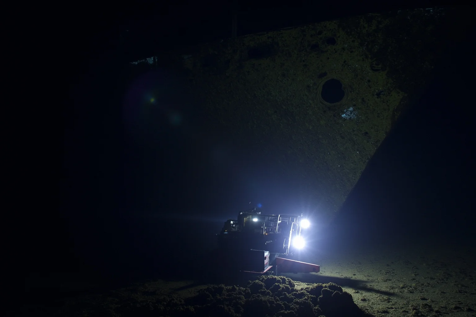22 Coolest Underwater Discoveries Made Throughout History 11 Deep-sea remotely operated vehicle with lights approaching a massive shipwreck on the dark ocean floor